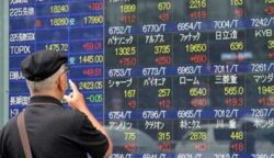Seorang warga melihat papan bursa saham di Jepang