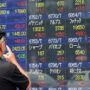 Seorang warga melihat papan bursa saham di Jepang
