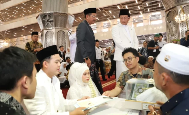 Infoaceh.net – Sebanyak 100 pasangan mengikuti prosesi nikah massal yang digelar di Masjid Istiqlal, Jakarta, Sabtu (28/6/2025). Acara ini menjadi bagian dari peringatan Tahun Baru Islam 1 Muharram 1447 Hijriah yang diselenggarakan oleh Kementerian Agama RI. Pantauan di lokasi, ratusan mempelai pria dan wanita tampak khidmat mengenakan busana adat dan pakaian muslim formal. Mereka duduk berdampingan di atas karpet merah masjid, didampingi wali serta keluarga masing-masing. Di depan mereka tertata kotak mahar dan dokumen nikah yang menjadi simbol keabsahan prosesi akad. Akad nikah berlangsung bergantian di bawah pengawasan para penghulu dari Kantor Urusan Agama (KUA). Prosesi berjalan tertib dan penuh haru. Menteri Agama Nasaruddin Umar yang hadir langsung menyampaikan apresiasinya terhadap antusiasme para peserta. Ia menyebut nikah massal ini bukan sekadar peristiwa administratif, melainkan momentum spiritual yang membawa berkah. “Insyaallah ini momen penuh berkah. Fasilitas sudah kami siapkan, termasuk kamar hotel untuk semua pasangan. Malam ini, silakan menikmati malam halal,” ujar Nasaruddin yang disambut gelak tawa para hadirin. Tak hanya akomodasi, beberapa pasangan juga mendapatkan bantuan modal usaha dari mitra penyelenggara. Nasaruddin berharap pernikahan massal ini menjadi awal kehidupan yang sakinah, baik di dunia maupun akhirat. “Pernikahan bukan hanya tanggung jawab duniawi, tapi juga hingga akhirat. Ibu-ibu, jangan takut disaingi bidadari surga, karena ibu-ibu yang salehah akan lebih cantik dari bidadari,” tambahnya dengan senyum. Program nikah massal ini ditujukan bagi masyarakat kurang mampu yang terkendala biaya. Pendaftaran dilakukan melalui KUA masing-masing hingga 20 Juni 2025. Seluruh fasilitas diberikan secara gratis, termasuk bimbingan perkawinan (Bimwin), buku nikah, serta suvenir resmi dari panitia. Direktur Jenderal Bimbingan Masyarakat Islam Kemenag, Abu Rokhmad, menegaskan bahwa program ini bertujuan memberikan legalitas pernikahan baik secara agama maupun negara. “Kami ingin membuka akses pernikahan yang sah tanpa beban biaya, agar masyarakat bisa melangsungkan kehidupan rumah tangga dengan tenang dan resmi,” ujarnya. Suasana hangat, tawa haru, dan rasa syukur mewarnai seluruh rangkaian acara, menjadikan nikah massal ini sebagai salah satu peringatan Tahun Baru Islam yang paling membekas di hati para peserta dan keluarga.